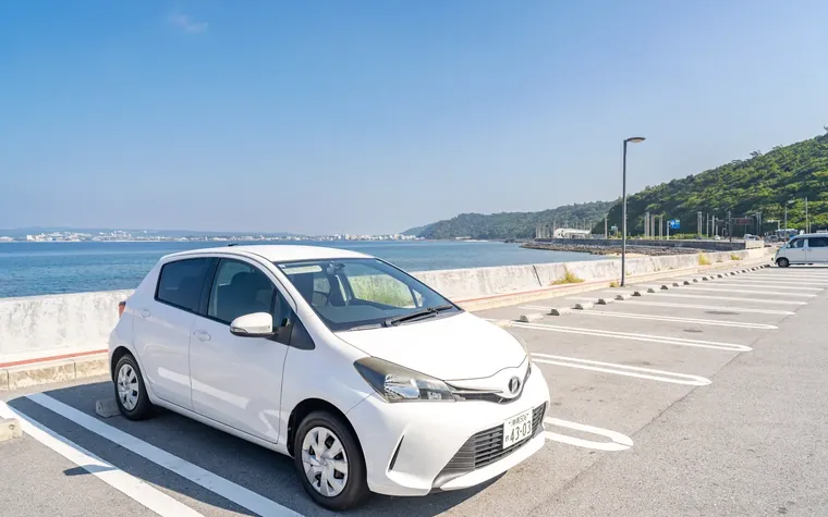 那覇空港ちかくの海沿いの道を走る White one のコンパクトカー